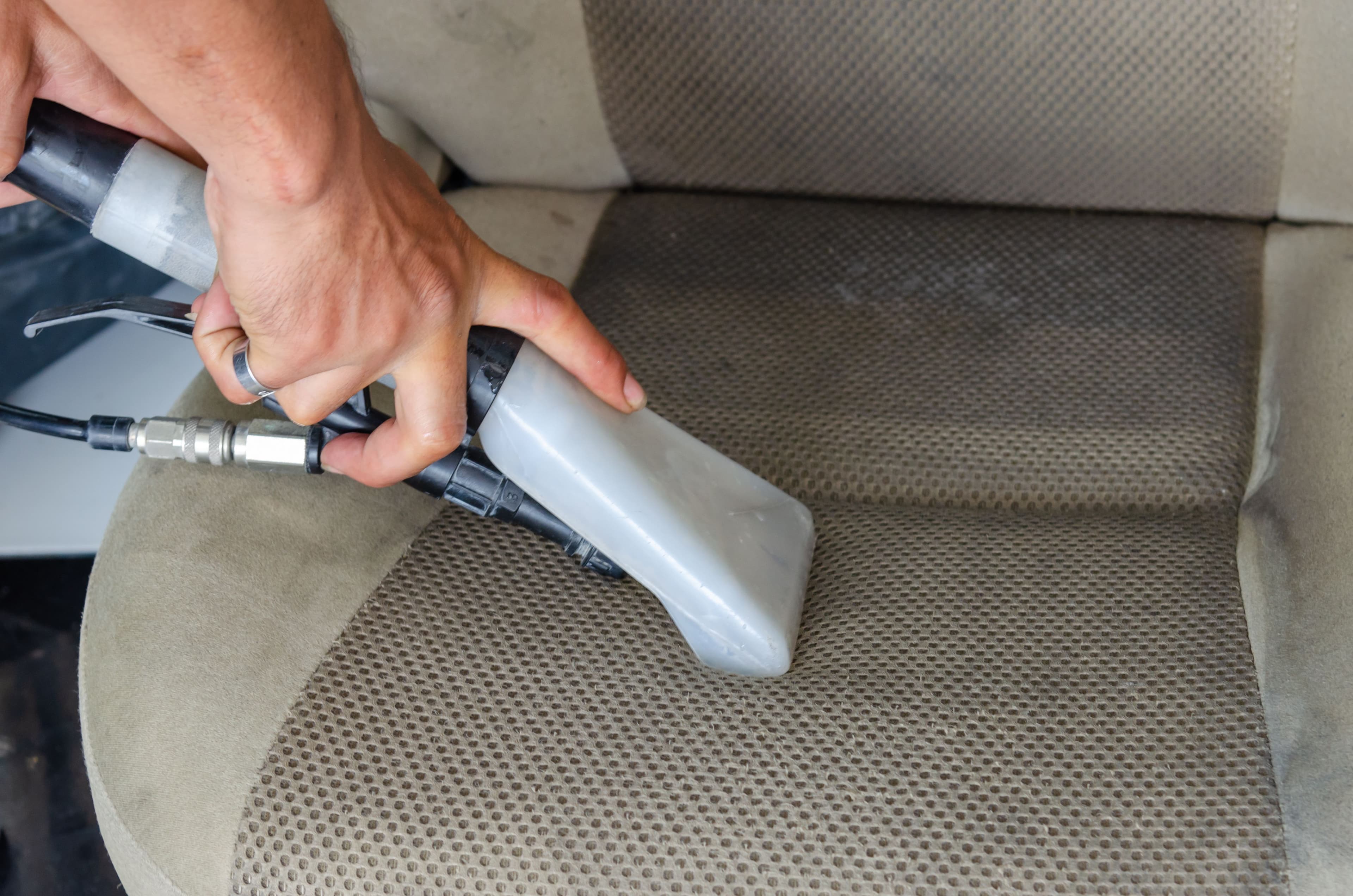 An extraction wand drawn across a fabric car seat, leaving a clean stripe through the soiled nap
