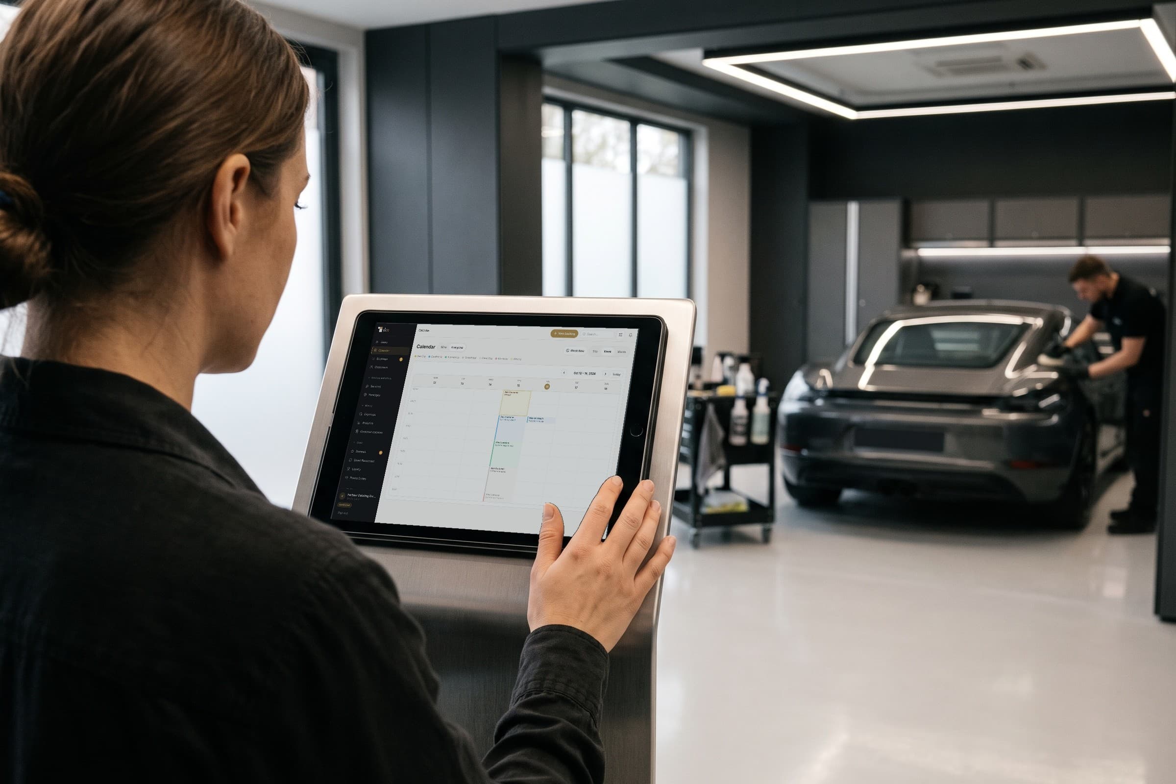 Responsável de um estúdio de detalhe automóvel consulta a agenda real do detailmasters num tablet, com um automóvel a ser preparado ao fundo.